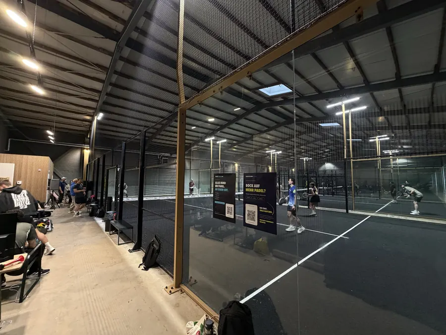 Ballwechsel in Welle 1, an der Scheibe Plakate von PadelCompass und Elevation Padel