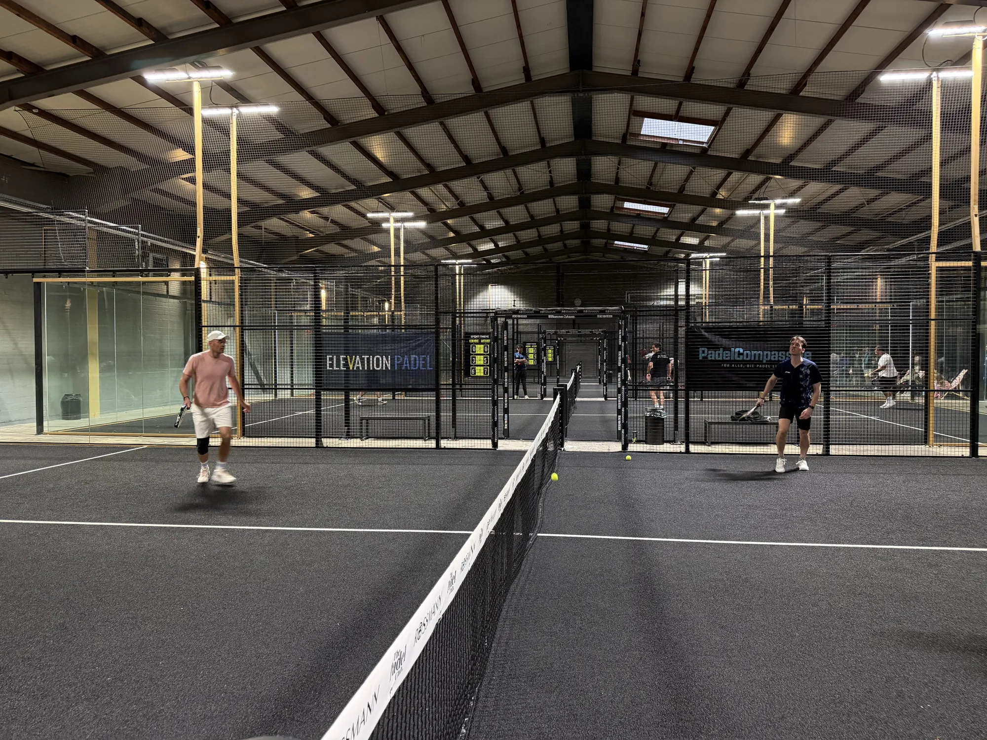 Blick über das Netz: Ballwechsel vor den Bannern von Elevation Padel und PadelCompass